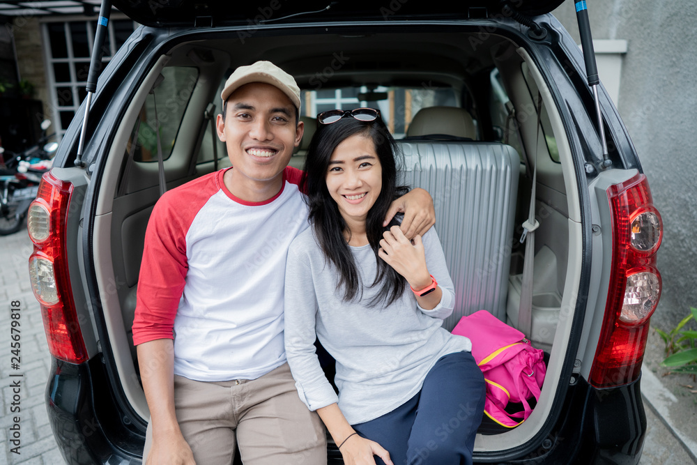 couple sitting on a car's trunk smiling together couple sitting on a car's trunk smiling together