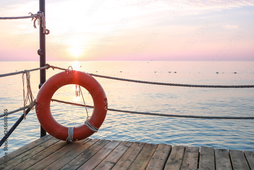 Red lifebelt on wooden pier on background of seascape at dawn.