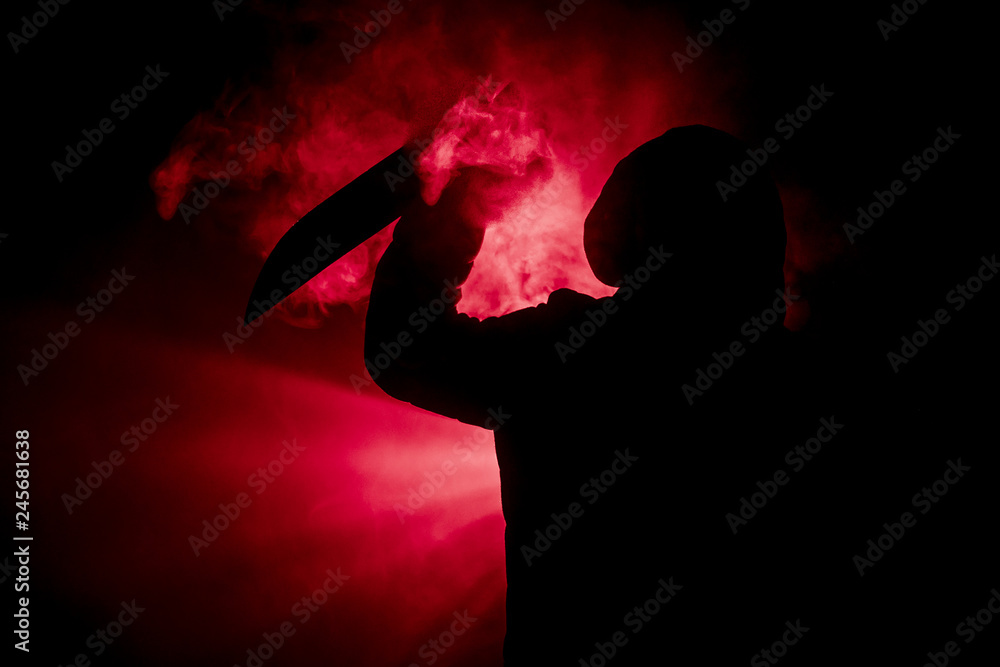 A dangerous hooded man standing in the dark and holding a knife. Face can not be seen. Committing a crime concept. Selective focus A dangerous hooded man standing in the dark and holding a knife. Face can not be seen. Committing a crime concept. Selective focus