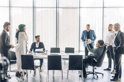 Debates or business solution concept. Multiracial business men in Arabian white national and formal European black clothes disputing at a meeting while sitting opposite each other at the modern office