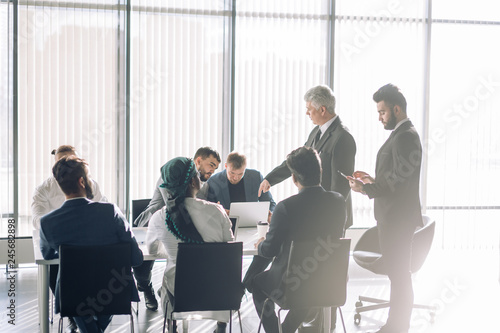 Mature old Chief Executive presents a young male speaker that is supposed to conduct a business presentation while standing in the board room with panoramic windows.