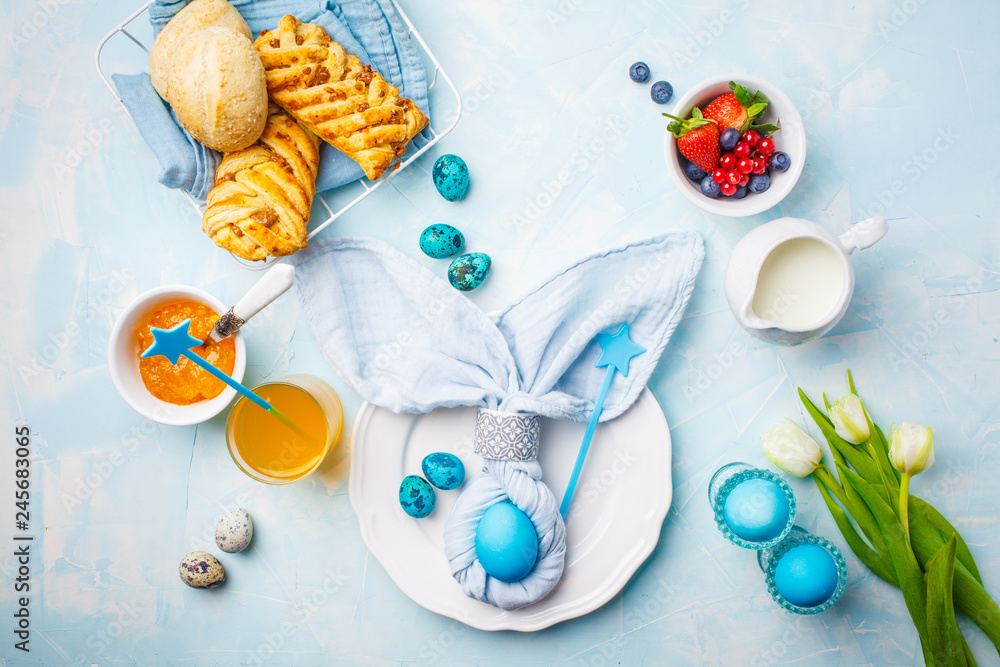 Easter Breakfast table. Colored eggs, buns, juice and jam. Blue background, top view, flat lay.