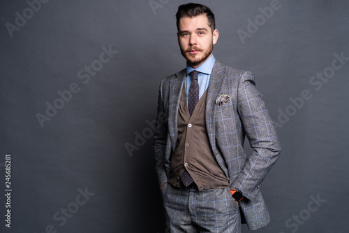A confident elegant handsome young man standing in front of a grey background in a studio wearing a nice suit.