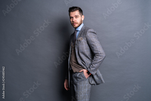 A confident elegant handsome young man standing in front of a grey background in a studio wearing a nice suit.