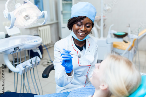 Female black dentist in dental office talking with female patient and preparing for treatment.