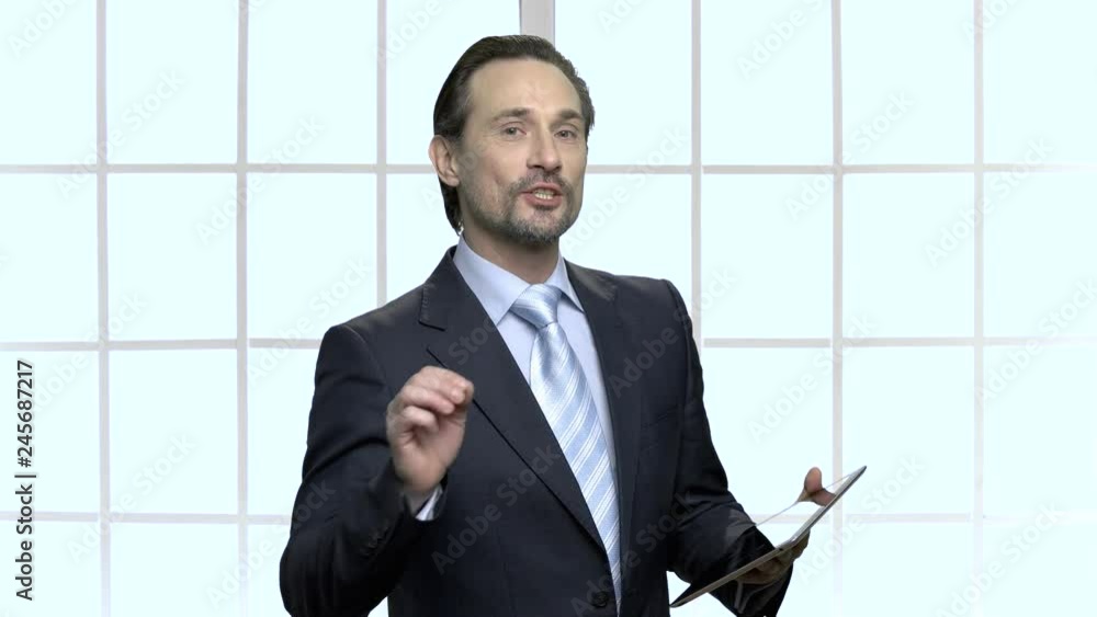 Mature business coach giving presentation. Confident executive holding digital tablet and speaking to employees at conference hall. Mature business coach giving presentation. Confident executive holding digital tablet and speaking to employees at conference hall.