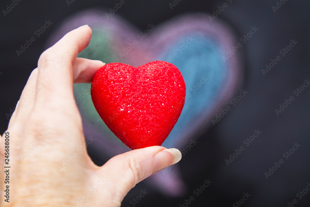 hand holding red heart with chalkboard background with drawings