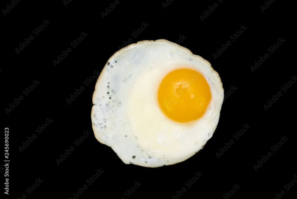 Top view of a sunny side up fried egg isolated on a black background in close-up Top view of a sunny side up fried egg isolated on a black background in close-up