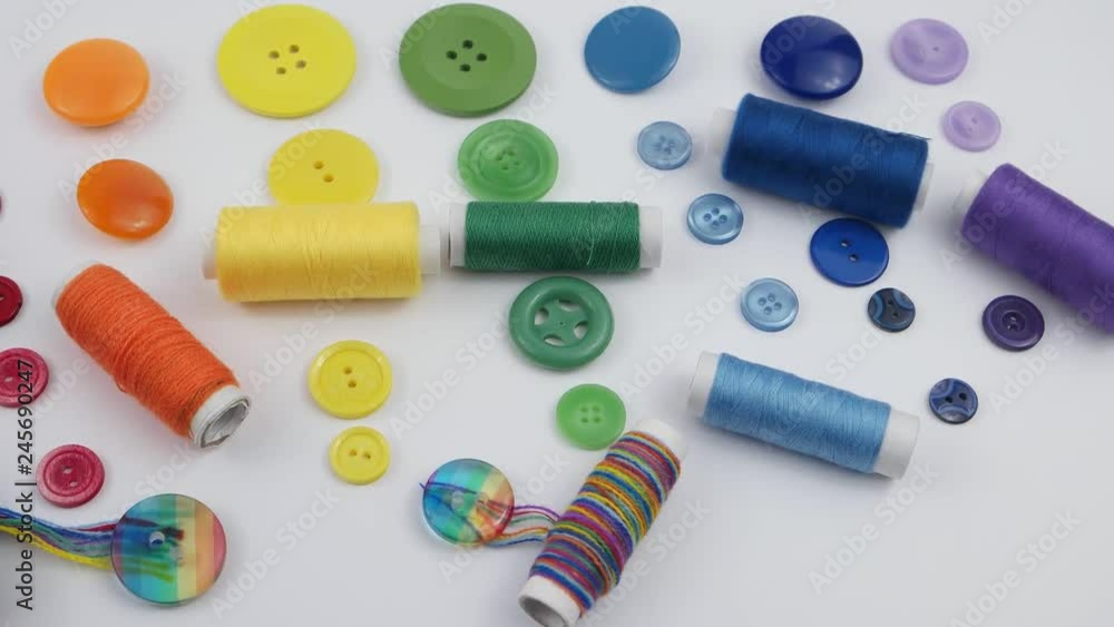 Composition of the sets of colorful buttons and spools of colorful thread are stacked in the spectrum of the colors of the rainbow on the white the background Composition of the sets of colorful buttons and spools of colorful thread are stacked in the spectrum of the colors of the rainbow on the white the background