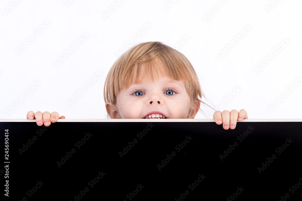 A little girl looks out from behind a black board. With blank space for text A little girl looks out from behind a black board. With blank space for text