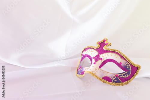 Photo of elegant and delicate pink, purple and gold venetian mask over white silk background.