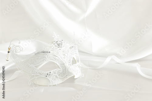 Photo of elegant and delicate white lace venetian mask over silk background.