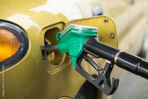 Yellow, gold car at a gas station being filled with fuel