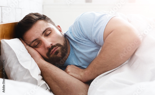Handsome young man sleeping in white bedding