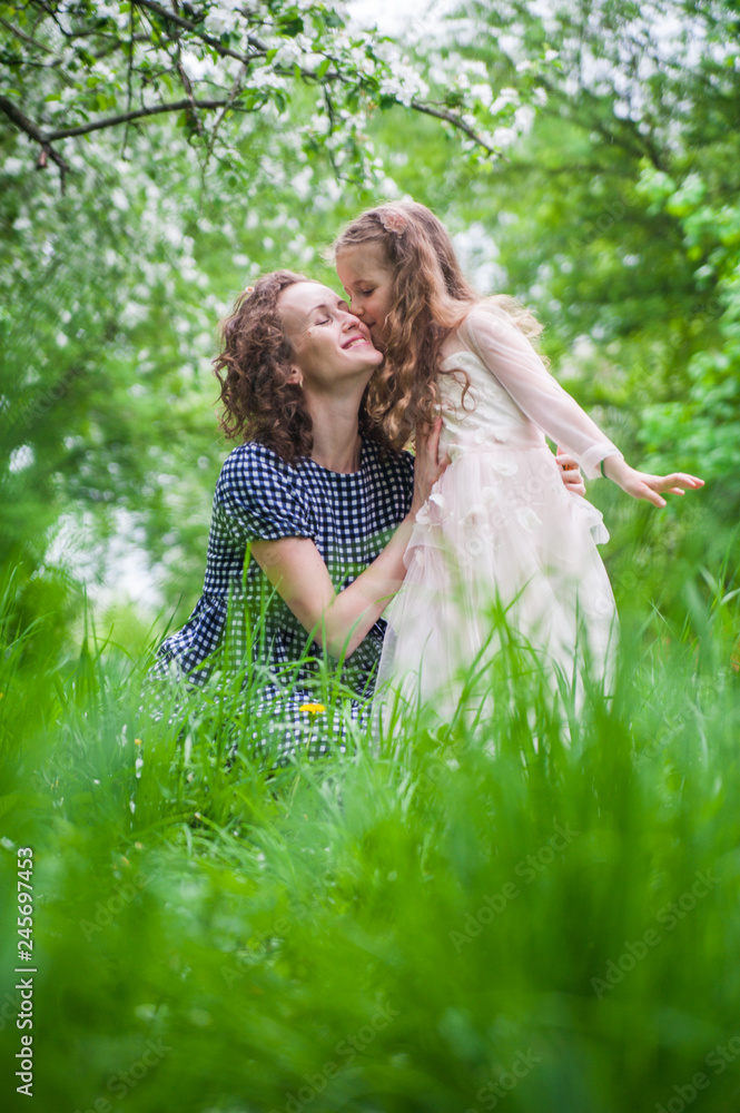 Blossoming garden. The mother and daughter. Girls in the garden. Mom kisses her daughter