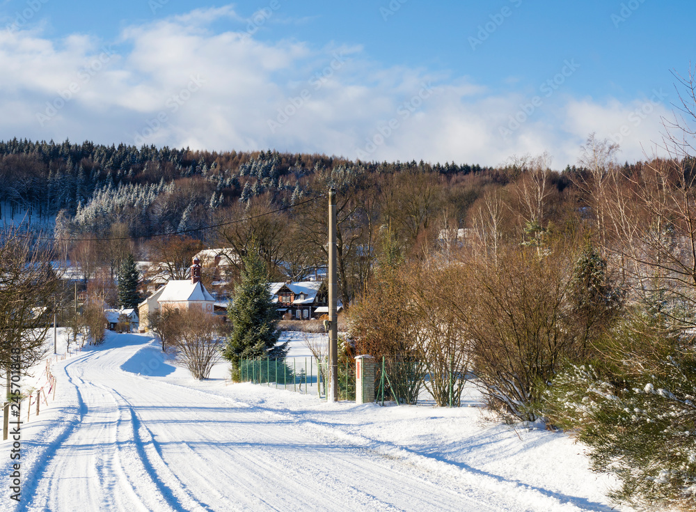 winter view on village travnik with chapel, timbered cottage and trees, snow covered rural landscape with in luzicke hory mountain