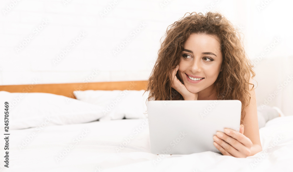 Cheerful young woman lying in bed with tablet Cheerful young woman lying in bed with tablet