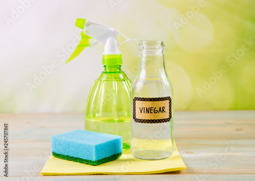 Chemical free home cleaner products concept. Using natural destilled white vinegar in spray bottle to remove stains. Tools on wooden table, green bokeh background, copy space. photo