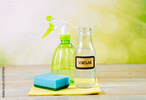 Chemical free home cleaner products concept. Using natural destilled white vinegar in spray bottle to remove stains. Tools on wooden table, green bokeh background, copy space. photo
