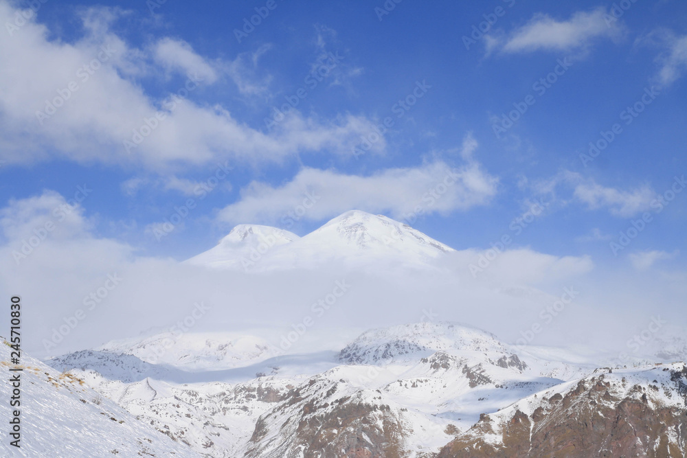 Two-headed Mount Elbrus among the clouds. View from Mount Cheget, Baksan valley, Kabardino-Balkaria, North Caucasus, Russia