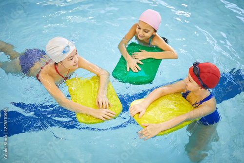 Group of girls having fun and swimming with board together in swimming pool