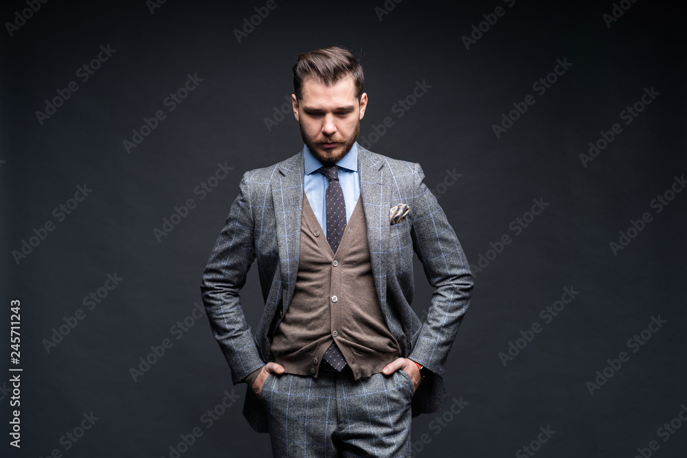 A confident elegant handsome young man standing in front of a black background in a studio wearing a nice suit.