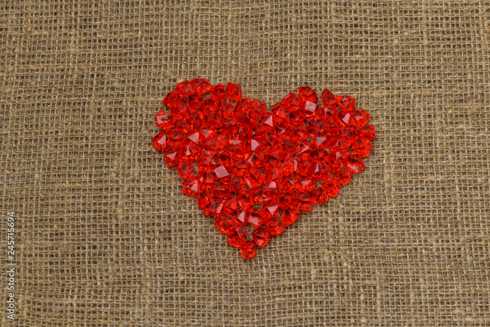 Valentine's day. A large red plastic glass heart of small crystals lies on a brown burlap (bag). Horizontal photography