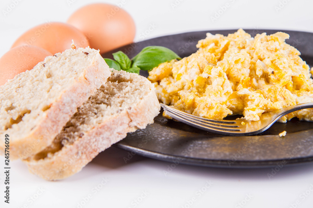 Scrambled eggs, some fresh eggs and wholemeal bread, and a fork, decorated with basil, on a white background Scrambled eggs, some fresh eggs and wholemeal bread, and a fork, decorated with basil, on a white background