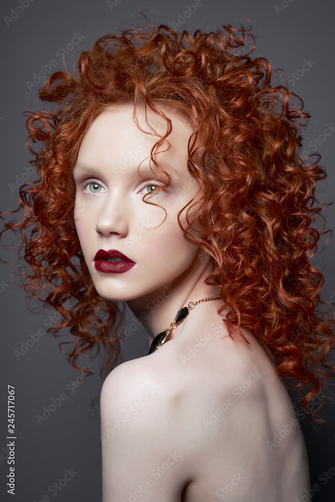 Fototapeta premium Beautiful young woman with red-hair on grey background. Nude pretty lady with bright red lipsstick and modern art makeup. Sensual model pose in photo-studio. Sexy naked body.