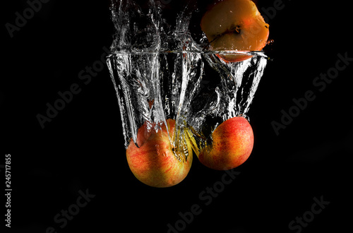 AApples falling in water with splash on black background.