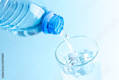 Pouring clean water from a plastic bottle. Glass of water in blue.