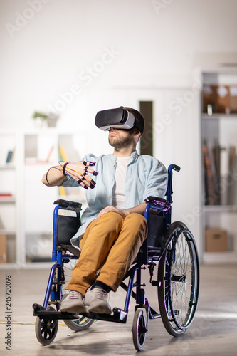Fotografie Young disable man with sensors on fingers and vr headset sitting in wheelchair w