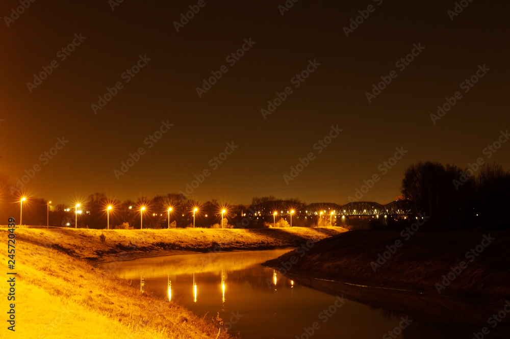 Country night landscape. Water channel. Illuminated lanterns along the river bank. Yellow warm light falls on the water surface. Night landscape. Summer night.