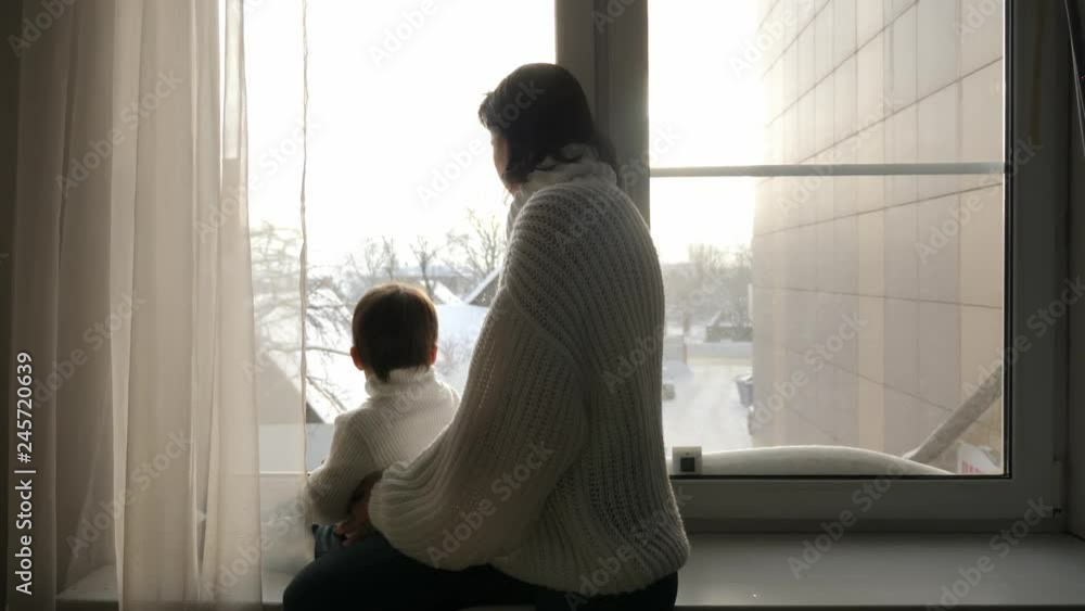 mom and son sitting on the big window of the house in the winter mom and son sitting on the big window of the house in the winter