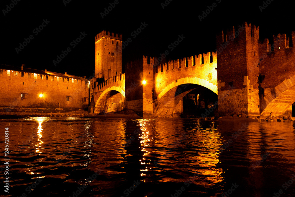 Castelvecchio bridge in Verona taken from the river during a winter evening illuminated by vintage lights