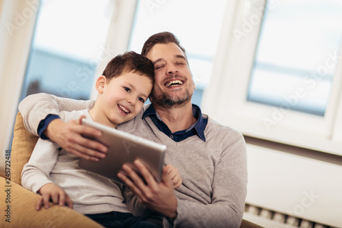 Father and son playing on a tablet at home, having fun, selective focus.
