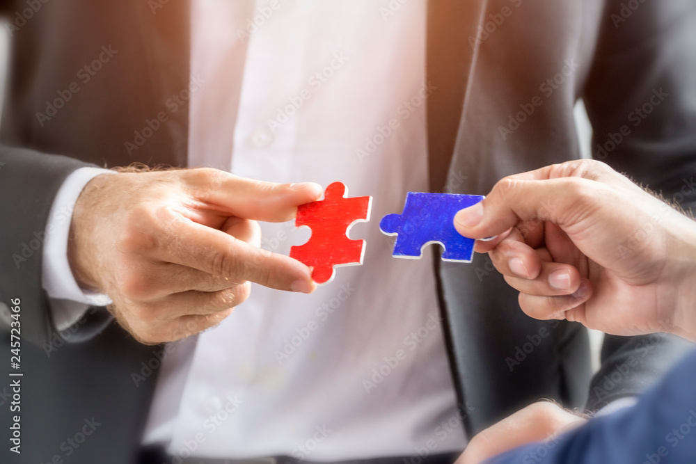 Partnership and teamwork in business strategy concept; Hand of two businessman are holding jigsaw puzzle connecting together.
