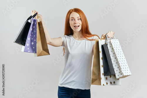 Beautiful young happy ginger woman holding shopping bags over ywhite background. close up shot. girl is crazy about shopping photo