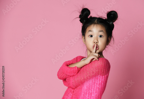 Asian kid girl in pink sweater shows shh sign Close up portrait photo