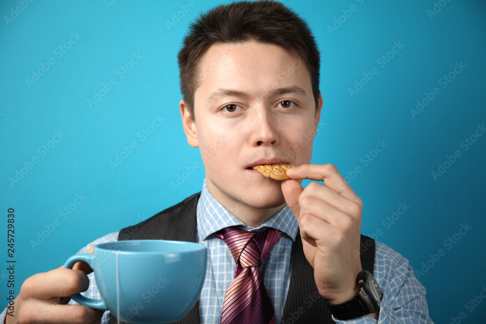 Businessman with a big cup of tea and cookies on a blue background. Breakfast in the office. Businessman with a big cup of tea and cookies on a blue background. Breakfast in the office.