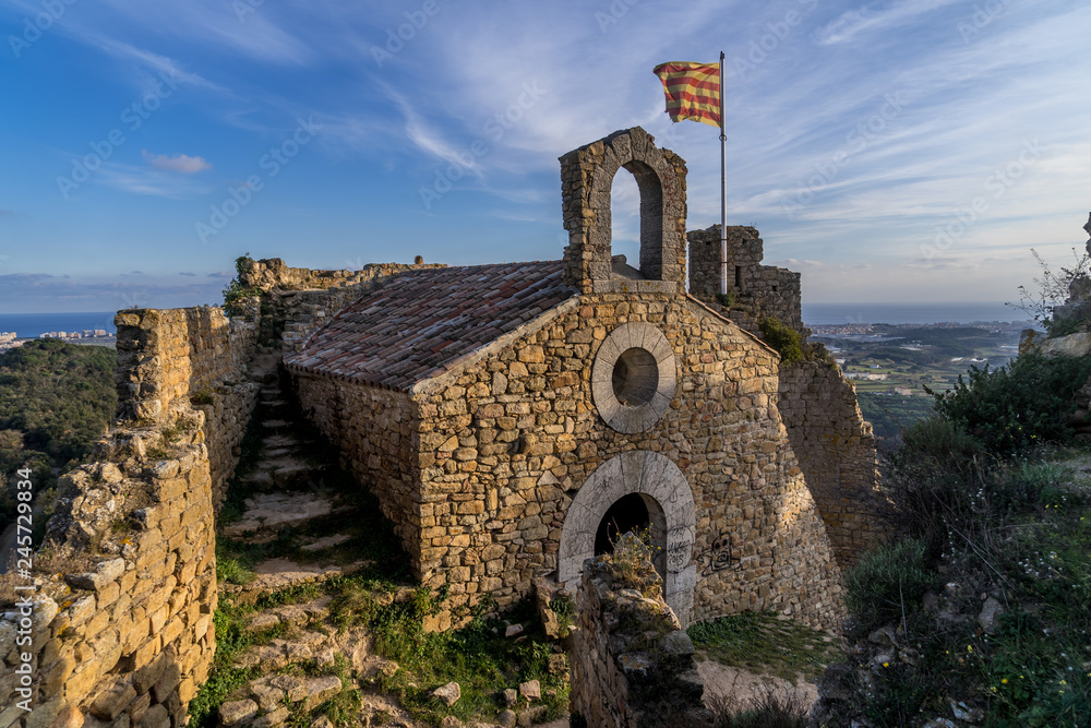 View of Palafolls castle medieval ruined stronghold between Girona and Barcelona on the Costa Brava with the Catalan flag proudly flying over the Romanesque church View of Palafolls castle medieval ruined stronghold between Girona and Barcelona on the Costa Brava with the Catalan flag proudly flying over the Romanesque church
