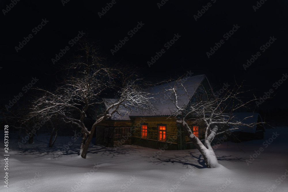 Russia, Night Winter Christmas Landscape With Old Snow-Covered Fairy Tale House Among Snowdrifts And Trees. Ancient Russian Old Wooden House With Glowing Red Windows On Epiphany ( Christening ) Night