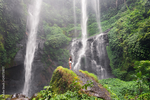 Fototapeta Naklejka Na Ścianę i Meble -  slender girl standing in front of a waterfall on a rock