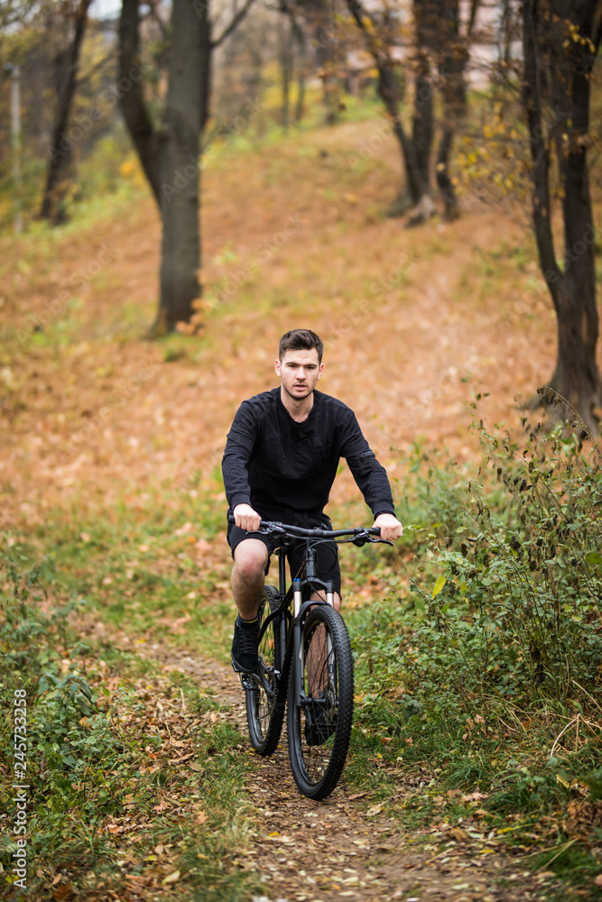 Naklejka premium Happy young cyclist man ride on his bicycle on a training in autumn forest