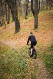 Young man in black t-shirt on sports bike against the background of the autumn city park, concept of healthy lifestyle, copy space.