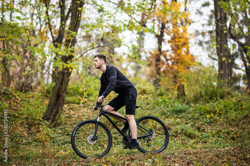 Young handsome sport man with his bike training in park in autumn time, with colorful background