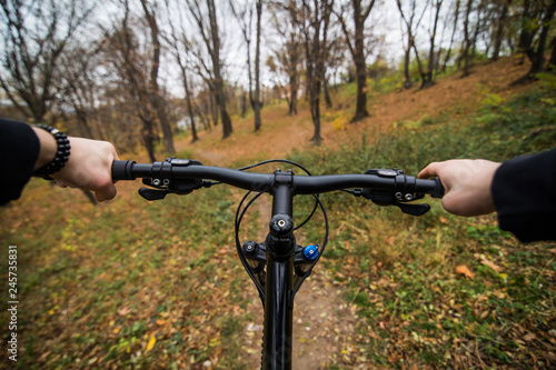 Close-up image of cyclist man hands on handlebar riding mountain bike on trail in autumn park © dianagrytsku
