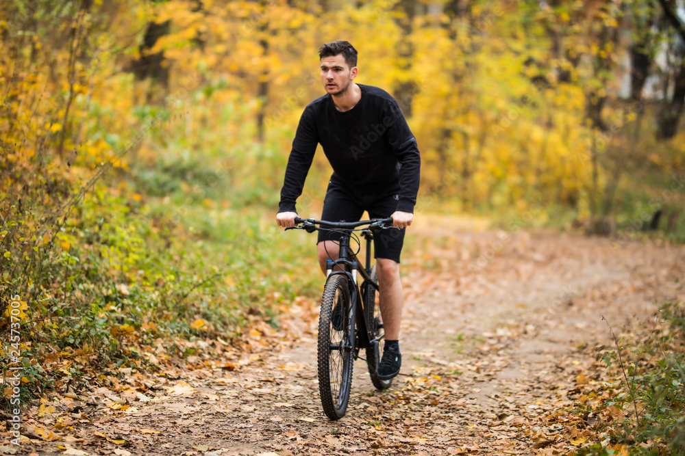 Fototapeta premium Handsome man biker in cycling clothing training on bicycle, getting ready for race in park on fresh air. Man enjoying morning bike ride. Concept of motivation, healthy lifestyle