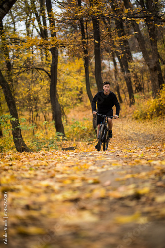 Young athlete ride with bicycle on the autumn park. Preparing for training