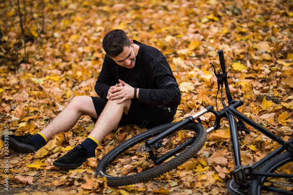 Active young man holding by his hurt or broken leg while lying on